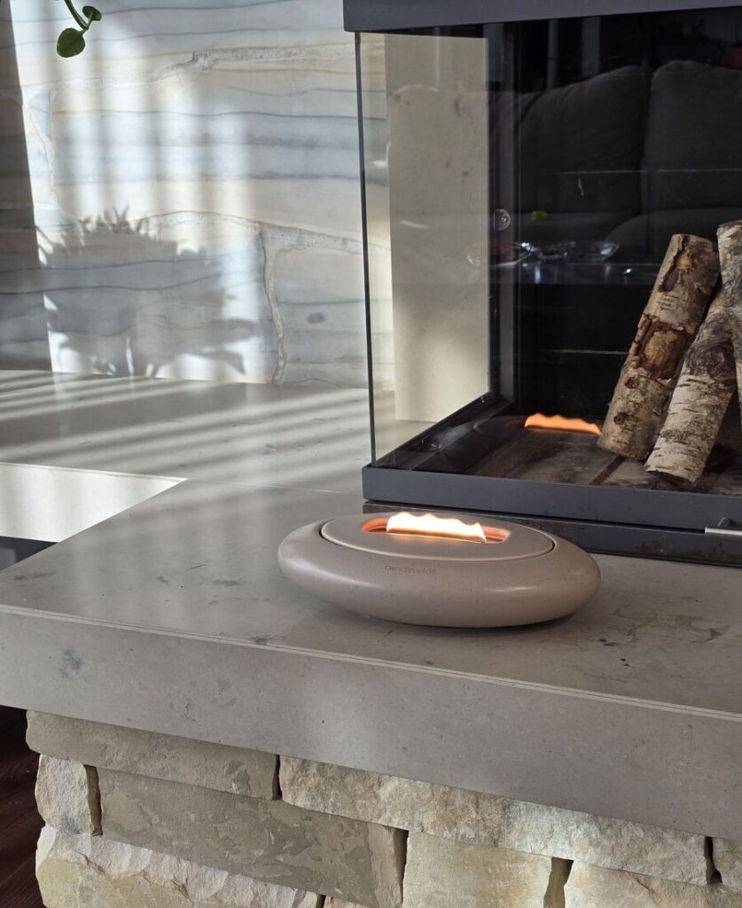 Candlewide Umber Beige ceramic refillable candle with a unique wide flame in front of fireplace.