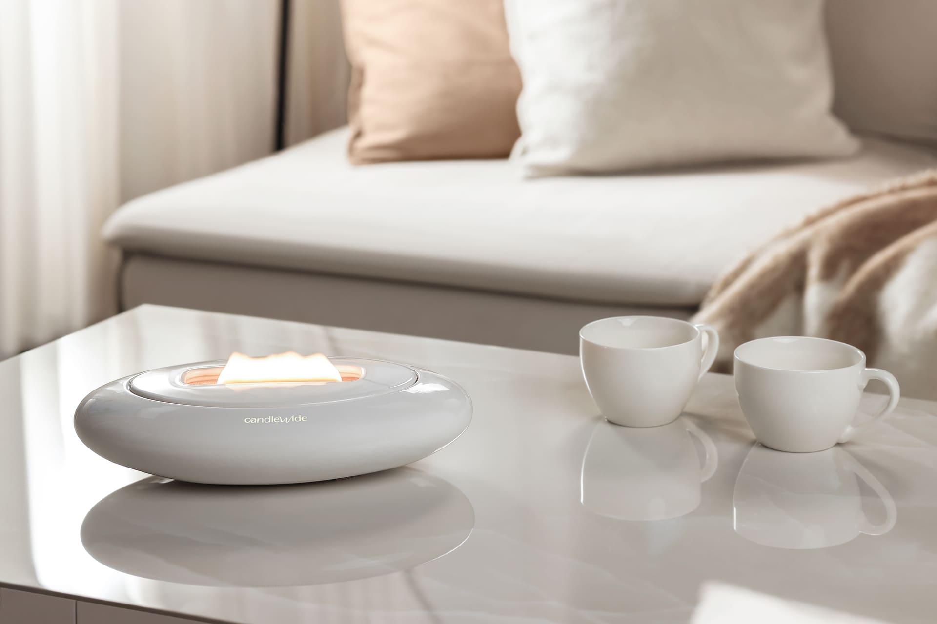 Candlewide ceramic Alabaster White refillable Candle with a unique wide flame, placed on a living room table next to two white cups.