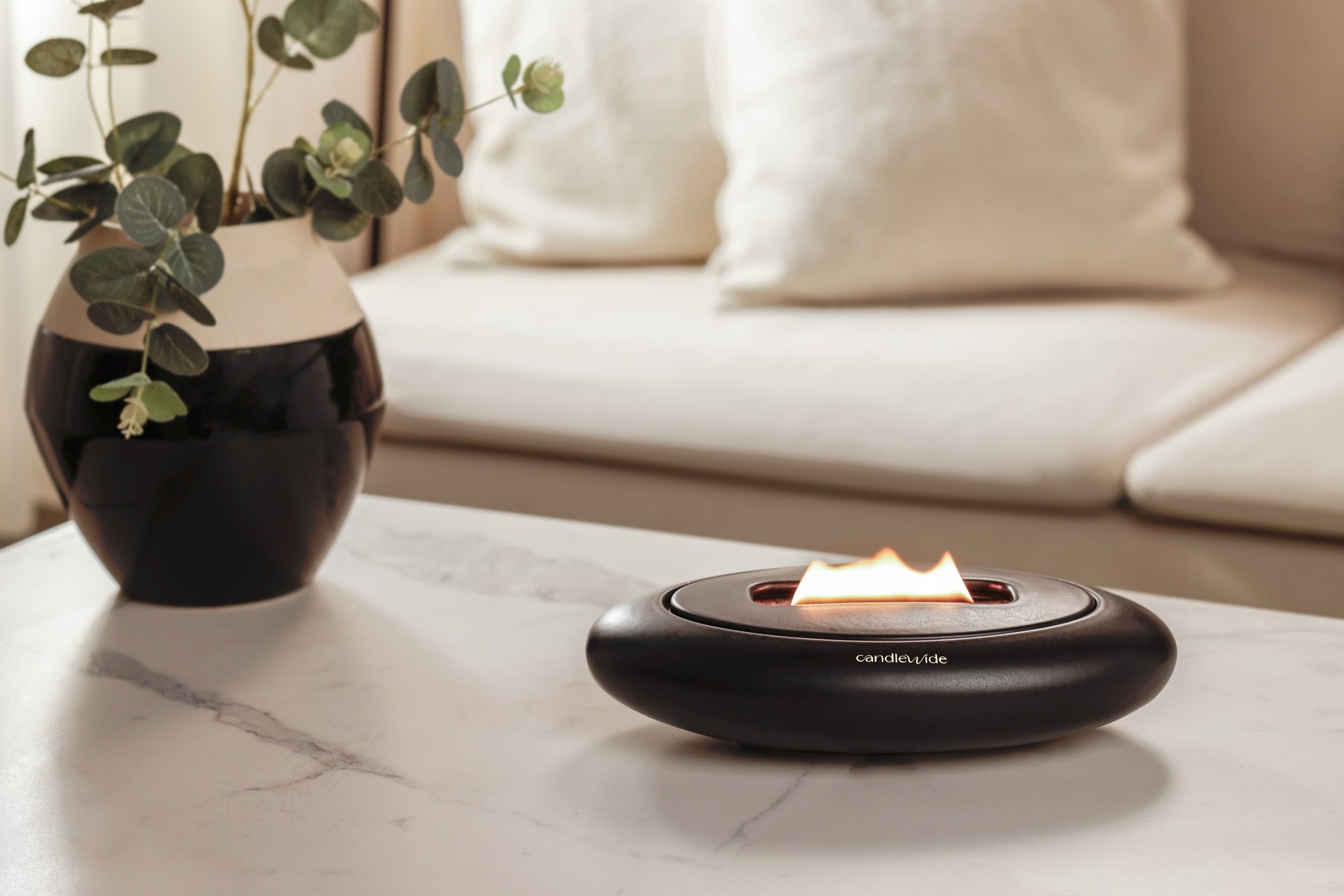 Candlewide Onyx Black ceramic refillable candle with a wide flame, placed on a living room table.