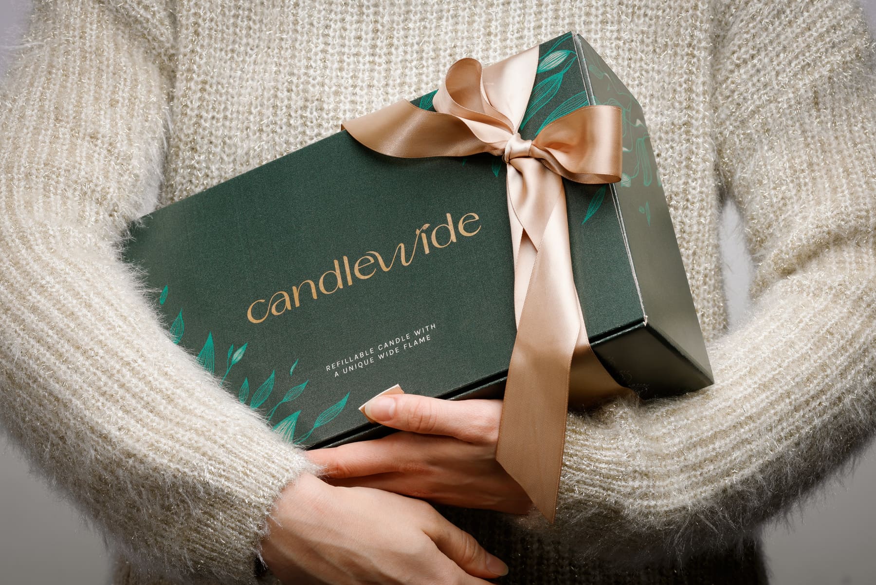 A person holding a Candlewide dark green gift box tied with a satin ribbon.