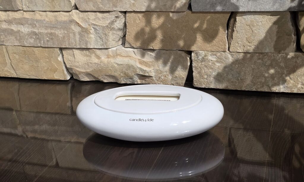 White Candlewide ceramic candle resting on a reflective surface in front of a natural stone wall, designed as a long-lasting interior element